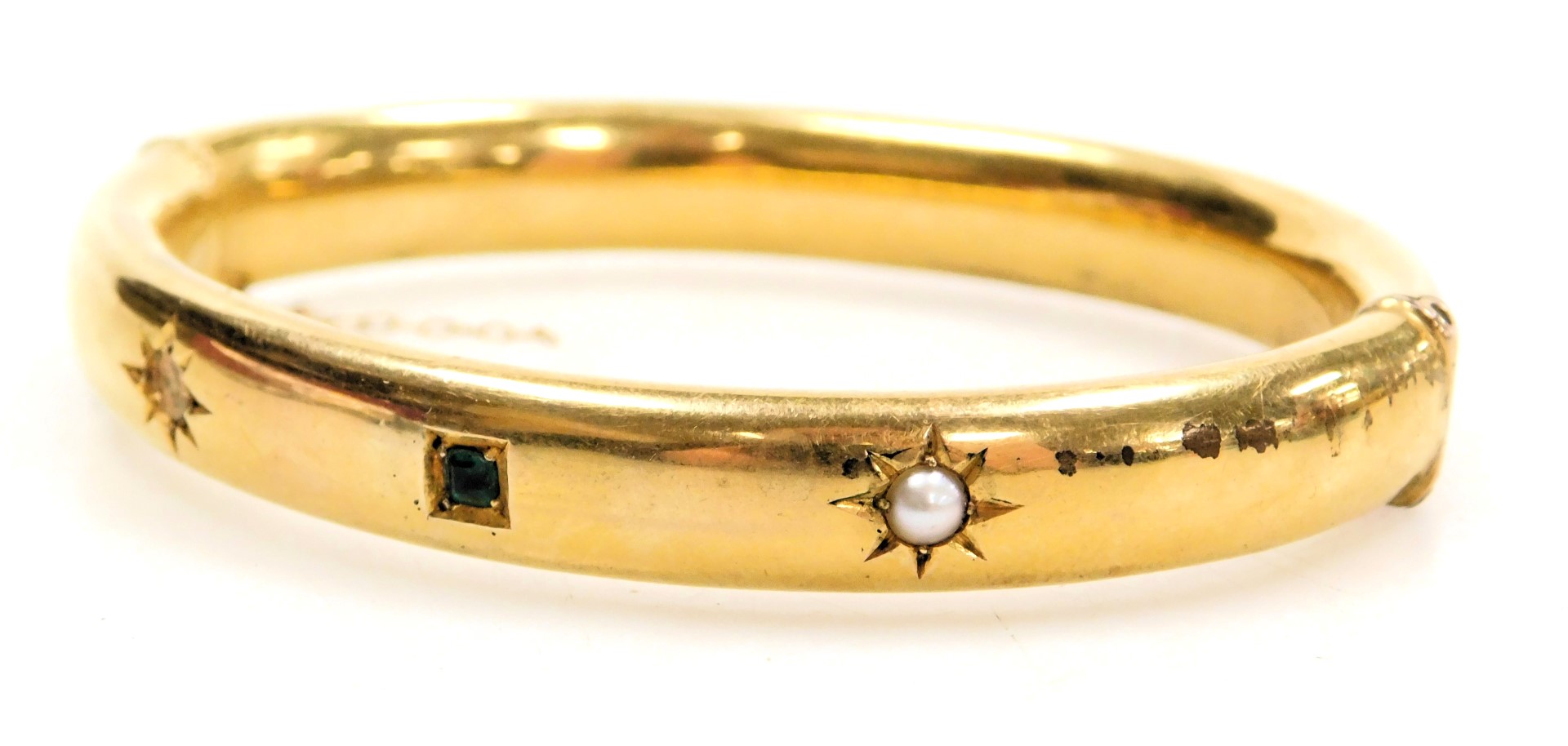 A seed pearl and emerald set bangle, one pearl lacking, in yellow metal, on a snap clasp, with safet