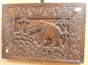 A carved wooden plaque, with elephant to central reserve, surrounded by scrolling foliage, 60cm x 41