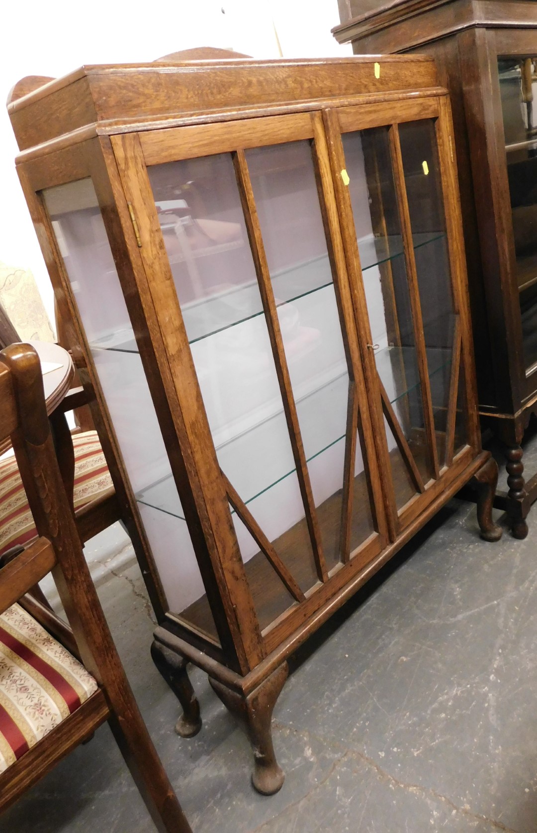 An early 20thC oak display cabinet, the raised shaped back above two glazed doors enclosing glass sh