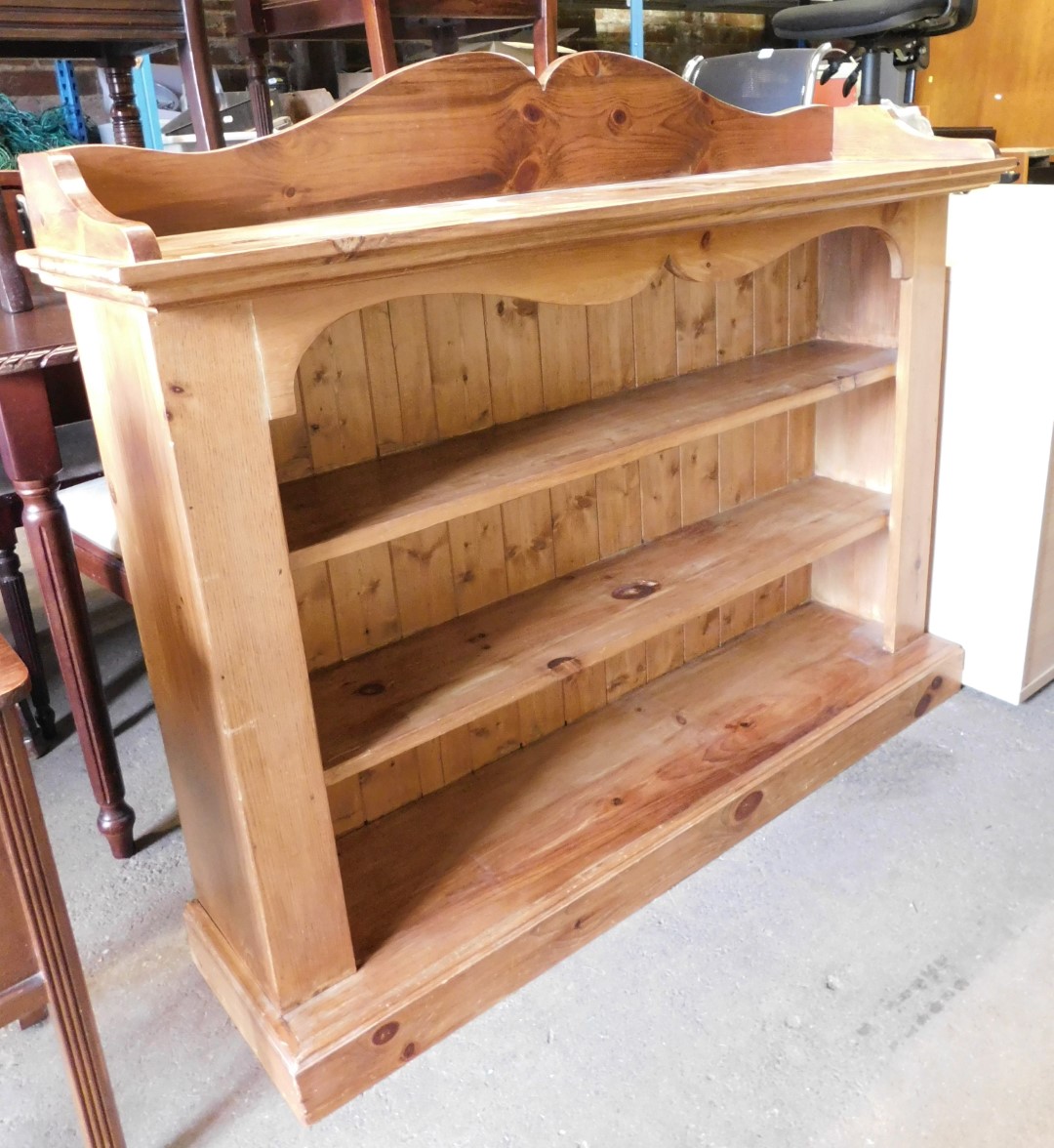 A pine open bookcase, the raised back above three central shelves, on a plinth base, 114cm high, 130