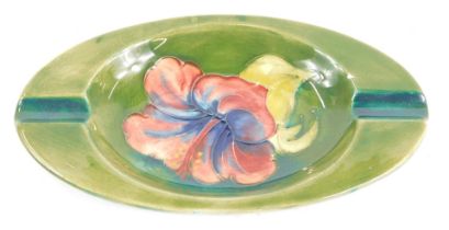 A Moorcroft pottery Hibiscus pattern ashtray, on a green ground, impressed marks, 15.5cm diameter.