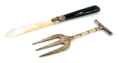 Two 20thC white metal trinkets, comprising a silver plated meat fork, and a mother of pearl green ag