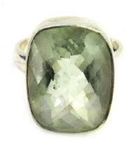 A dress ring, with a rectangular cut and faceted pale green stone, in a rub over white metal border