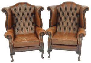 A pair of brown leather wing back armchairs, with button back, stud work and moveable seat, on mahog