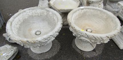 A pair of reconstituted stone urns, each of circular form with leaf moulded decoration, on a circula