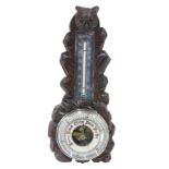 An early 20thC Black Forest style carved aneroid barometer, with owl shaped crest, and silvered ther