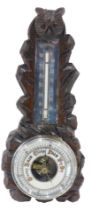 An early 20thC Black Forest style carved aneroid barometer, with owl shaped crest, and silvered ther