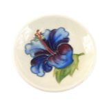 A Moorcroft pin dish, on a cream ground with central blue flower, stamp to underside, 8cm diameter.