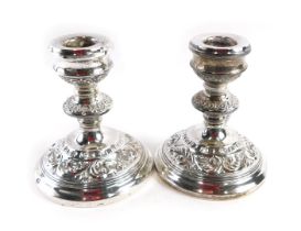 A pair of Elizabeth II silver squat candlesticks, with embossed rococo scroll design, on weighted ba