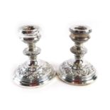 A pair of Elizabeth II silver squat candlesticks, with embossed rococo scroll design, on weighted ba