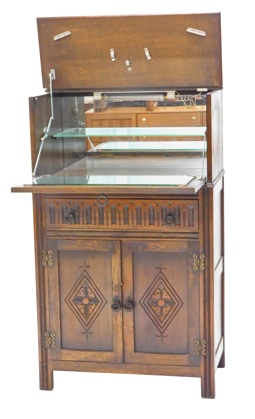 An Old Charm style oak cocktail cabinet, the double hinged top enclosing a mirrored interior, carved