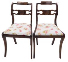 A pair of Regency dining chairs, each with a carved back, drop in seat, on sabre legs.