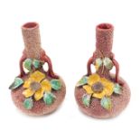 A pair of Continental Majolica two handled vases, each with flower encrusted decoration, on a red gr