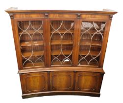 A mahogany convex shaped bookcase, the moulded dentil cornice above three glazed doors enclosing she