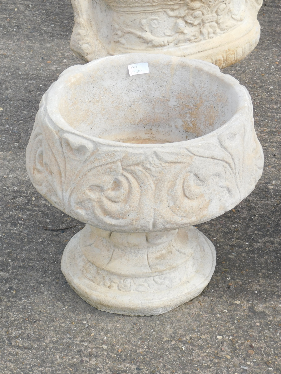 A reconstituted stone fleur de lys pattern urn, stylised with three petal design, on a circular foot