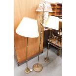 Three brass standard lamps, comprising one with arched top and cream and red shade, 150cm high, each