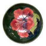 A Moorcroft pottery Hibiscus pattern bowl, green ground, impressed marks and paper label, 14cm wide.