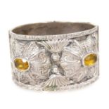 A Continental bangle, white metal, embossed in a floral and foliate design, set with four yellow sto