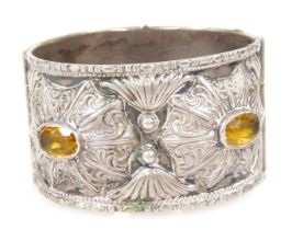 A Continental bangle, white metal, embossed in a floral and foliate design, set with four yellow sto
