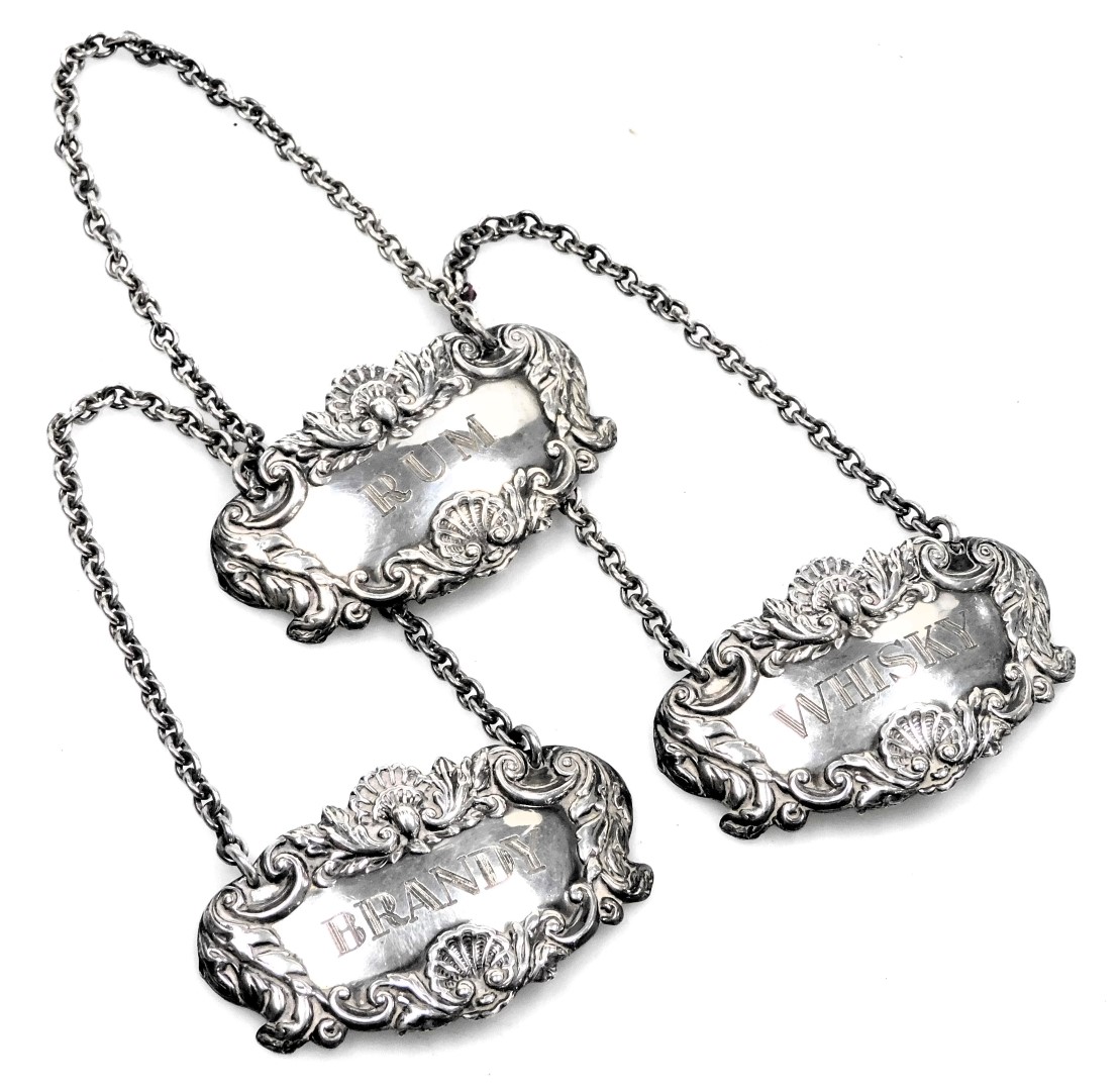 Three Elizabeth II silver decanter labels, with chain suspensions, and embossed foliate scroll and s