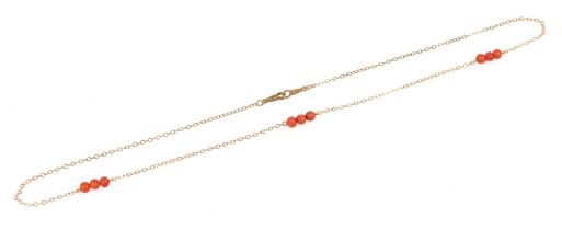 A 9ct gold cable link neck chain, set with three sets of three coral beads, at intervals, on a clip