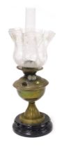 An early 20thC brass oil lamp, raised on a glass socle, with glass chimney and floral etched frilled