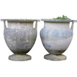 A pair of reconstituted stone two handled garden urns, of amphora style, on a circular plinth, 52cm