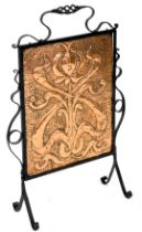 A late 19th/early 20thC wrought iron and embossed copper fire screen, decorated with a tulip and sty