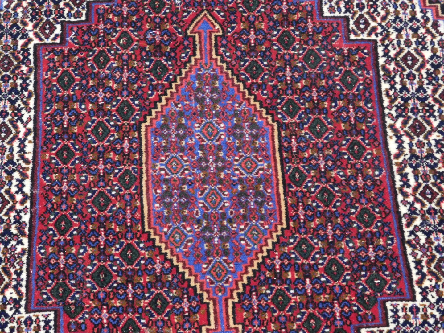 A Persian rug with a central medallion, surrounded by geometric motifs in red, cream pink and blue, - Image 2 of 3