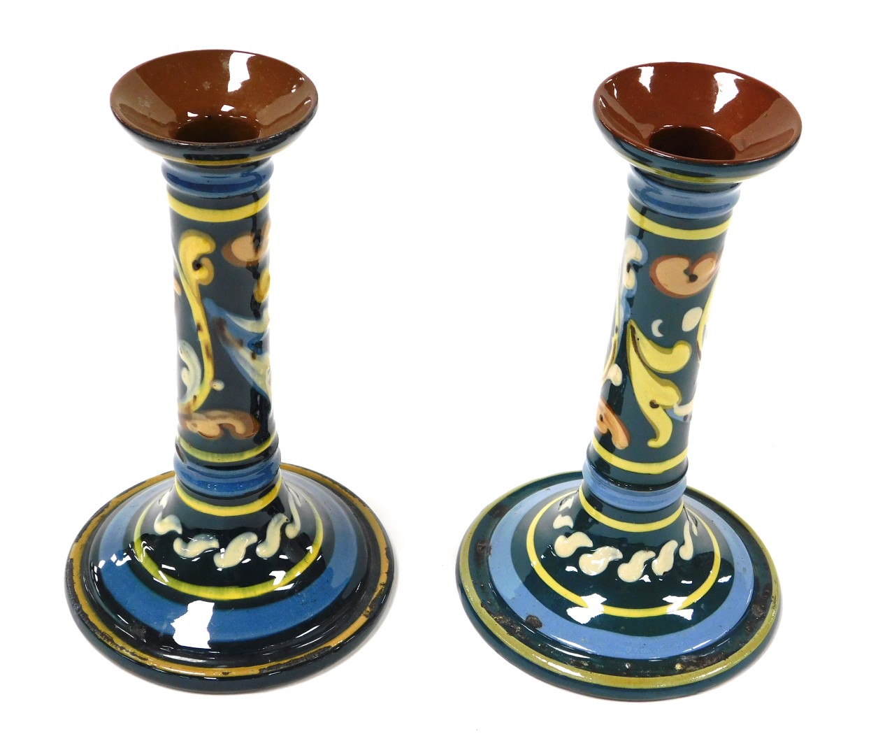 A pair of early 20thC Aller Vale Torquay pottery candlesticks, painted with scrolling foliate decora
