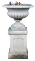 A reconstituted stone garden urn, of part fluted form, on a rectangular plinth with panelled sides,