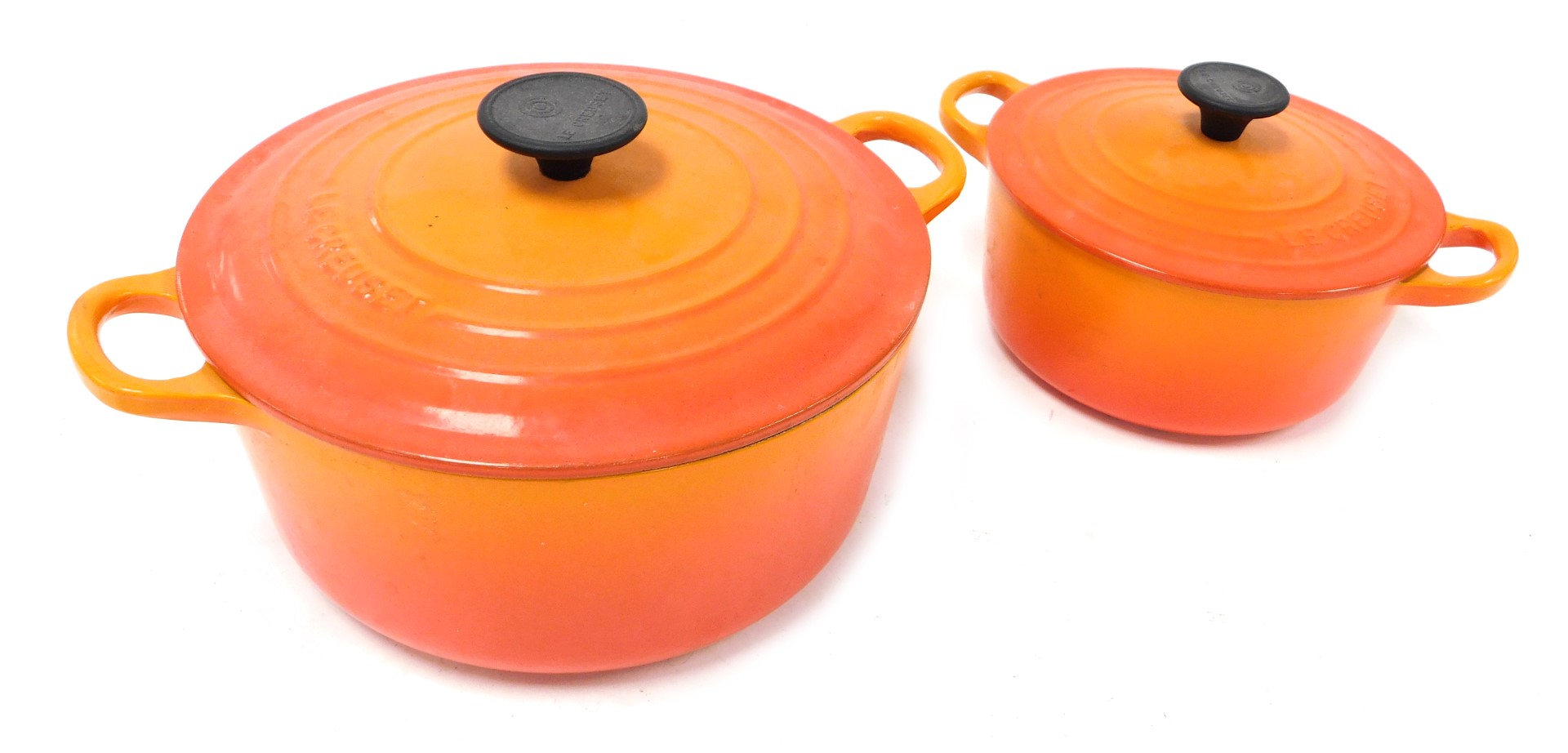 A pair of graduated orange enamel Le Crueset casserole dishes with lids.