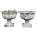 A pair of reconstituted stone garden urns, each cast with leaves, on a square base, 43cm high, 48cm