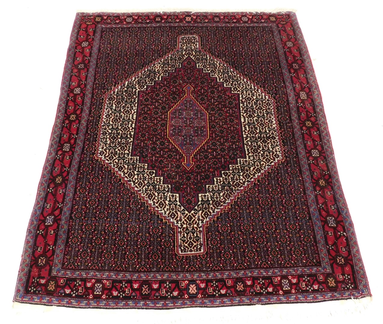 A Persian rug with a central medallion, surrounded by geometric motifs in red, cream pink and blue,