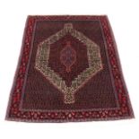 A Persian rug with a central medallion, surrounded by geometric motifs in red, cream pink and blue,