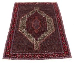 A Persian rug with a central medallion, surrounded by geometric motifs in red, cream pink and blue,