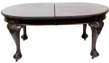 An early 20thC mahogany extending dining table, the oval top a dragooned border, on scroll and leaf