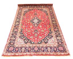 A Persian rug decorated with leaves and scrolls, on a red ground, with one wide and two narrow borde
