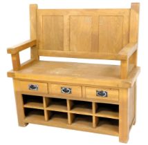 A light oak settle, with a panelled back, plain arms above an arrangement of three drawers and eight
