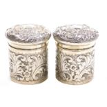A pair of Edward VII silver dressing table jars and covers, with embossed floral and foliate scroll