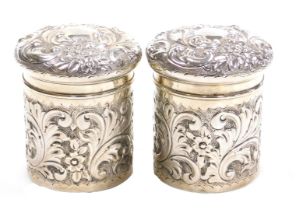 A pair of Edward VII silver dressing table jars and covers, with embossed floral and foliate scroll