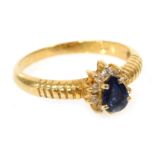 A lady's dress ring, set with a blue pear shaped stone, in a surround of white stones, in yellow met