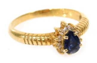 A lady's dress ring, set with a blue pear shaped stone, in a surround of white stones, in yellow met