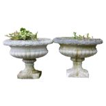 A pair of reconstituted part fluted garden urns, each on a square base, 43cm high, 56cm diameter.