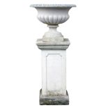 A reconstituted stone garden urn, of part fluted form, on a rectangular plinth with panelled sides,