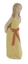 A Lladro porcelain figure, modelled as a young girl with arms clasp behind back holding hat, printed