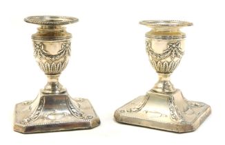 A pair of Victorian Adam style loaded silver dwarf candlesticks, embossed with urns, leaves and