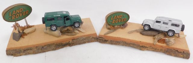 Two diecast Land Rover cars, in silver and green, each mounted on pieces of driftwood with Land