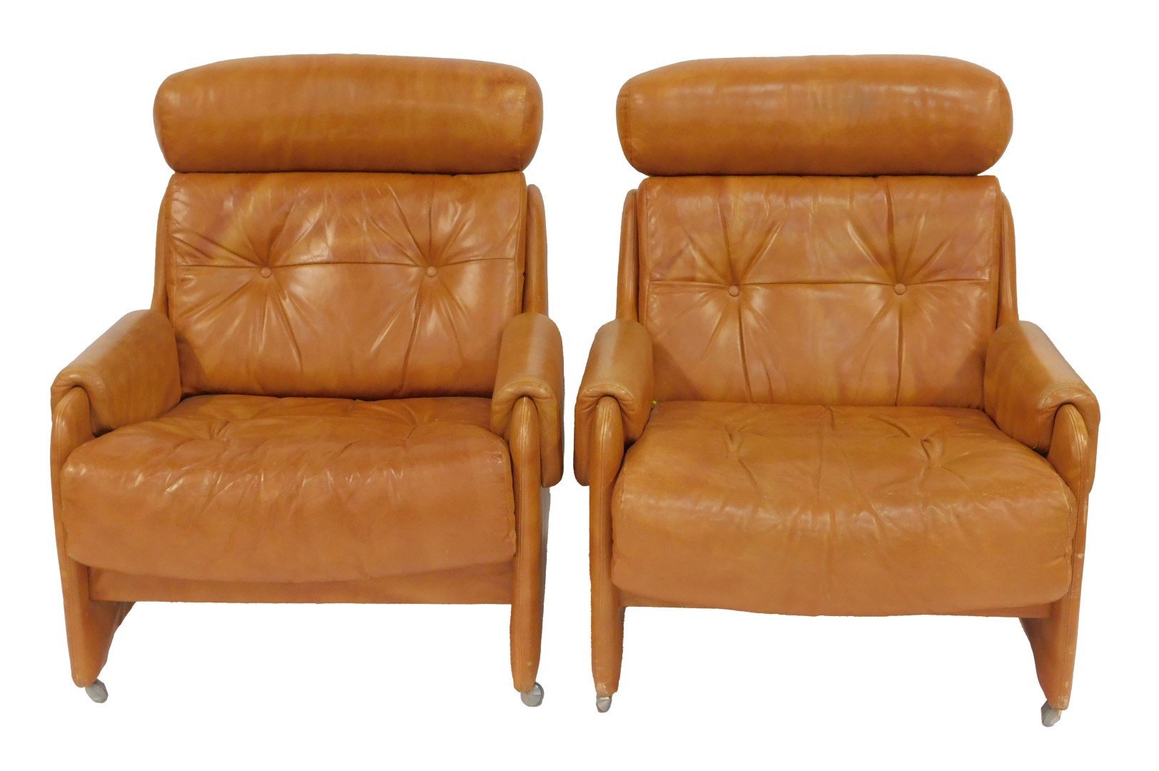 A pair of 1970s brown leather armchairs, each with a headrest, buttoned back and seat, on castors,