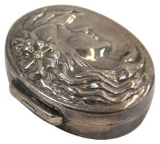 A silver pill box, the oval pill box with hammered decoration of a female with flowing hair and